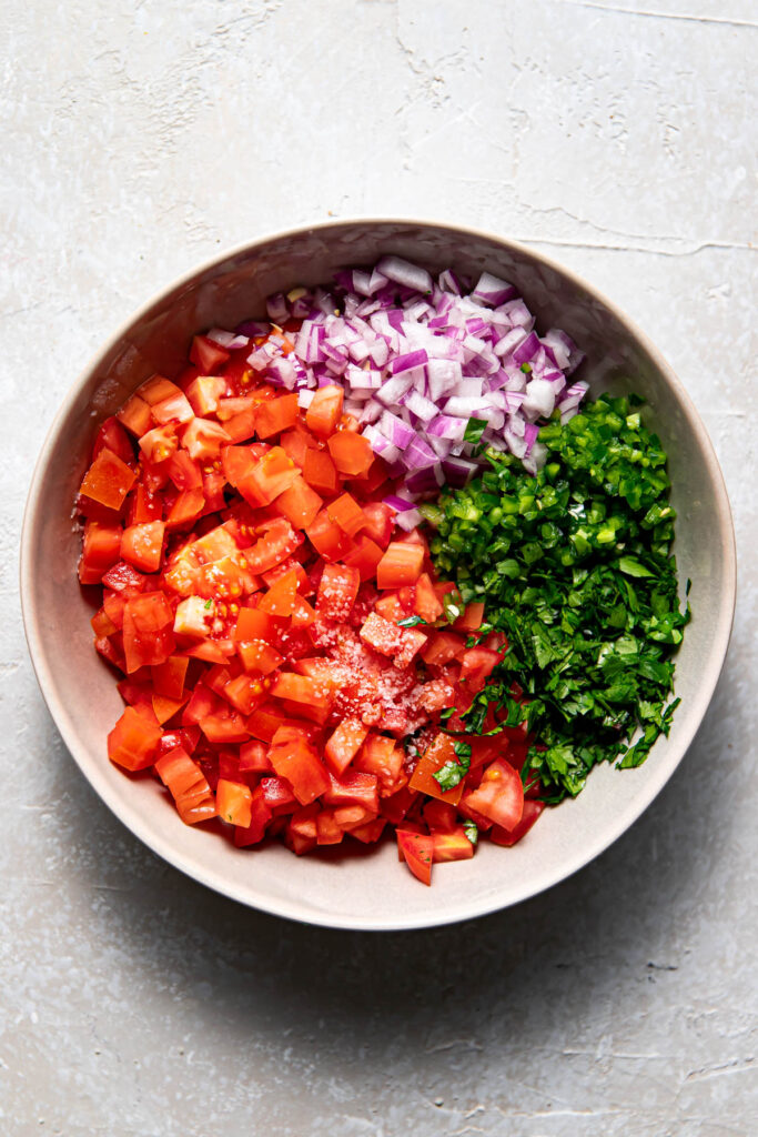 Bowl of tomatoes, red onion, jalapeno, lime, lemon and cilantro chopped up.