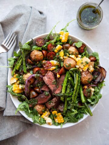 steak salad with chimichurri asparagus corn tomatoes onion in a white bowl