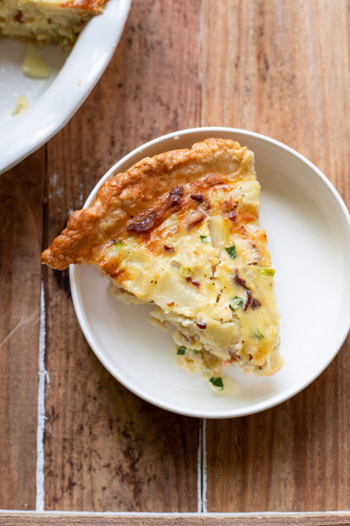 A hearty quiche made up of sliced potatoes, crispy pieces of bacon, green onion and a delicious cheesy sauce.