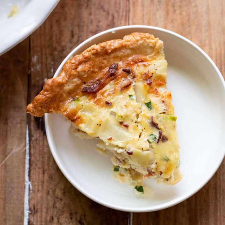 A hearty quiche made up of sliced potatoes, crispy pieces of bacon, green onion and a delicious cheesy sauce.