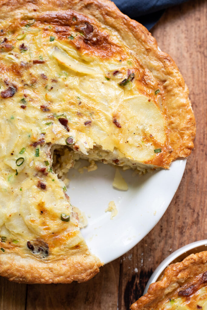 A hearty quiche made up of sliced potatoes, crispy pieces of bacon, green onion and a delicious cheesy sauce.