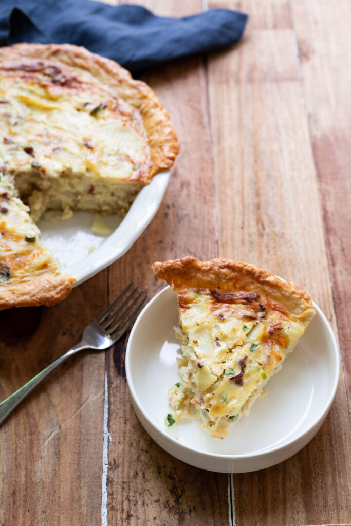 A hearty quiche made up of sliced potatoes, crispy pieces of bacon, green onion and a delicious cheesy sauce.  