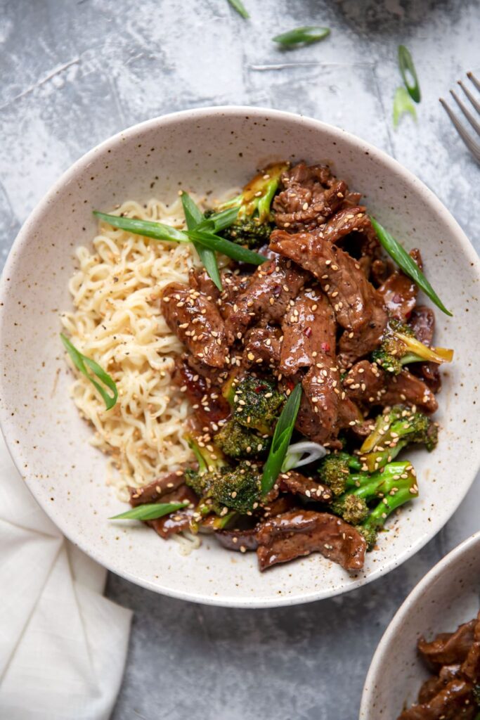 bowl of beef and broccoli with ramen noodles sesame seeds and green onions