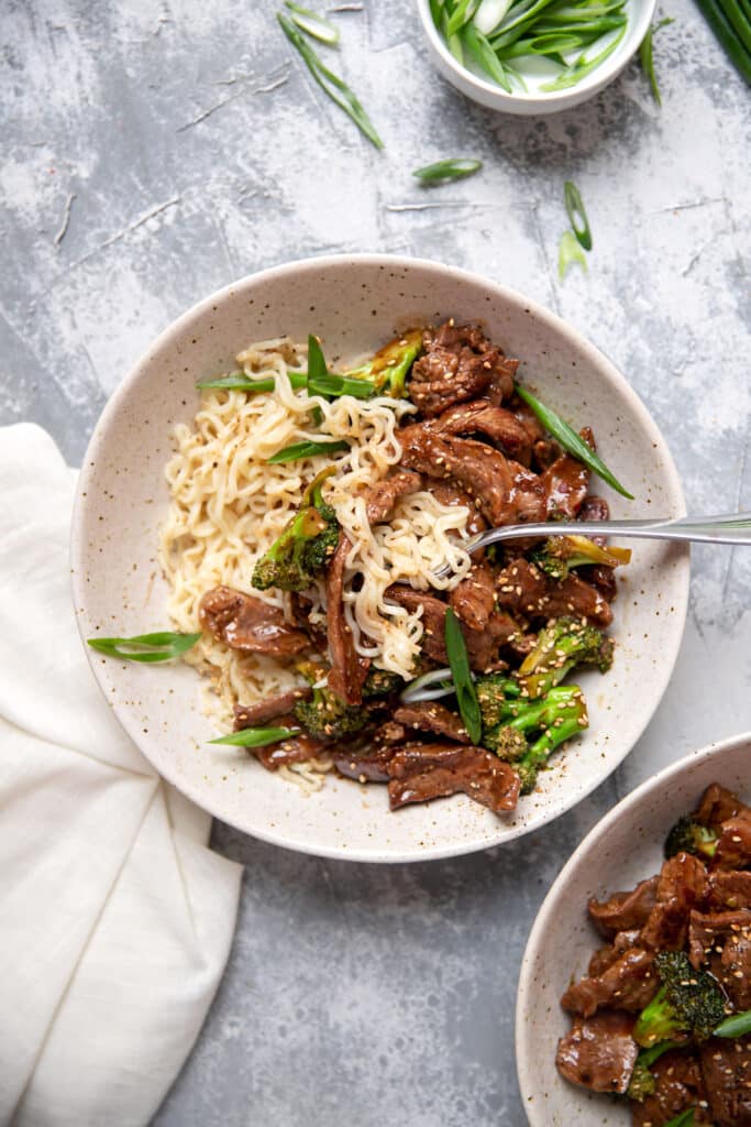 bowl of beef and broccoli with ramen noodles sesame seeds and green onions