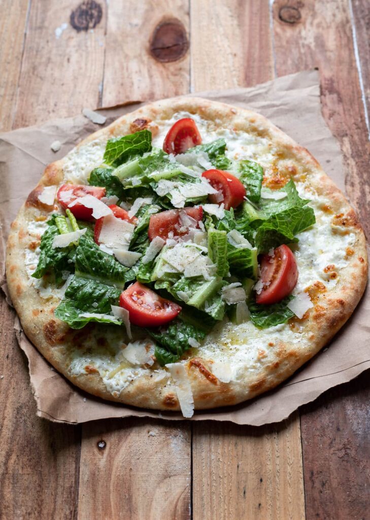 cheese pizza with caesar salad and tomatoes on top