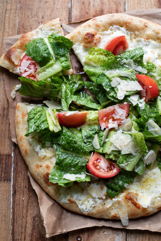 cheese pizza with caesar salad and tomatoes on top