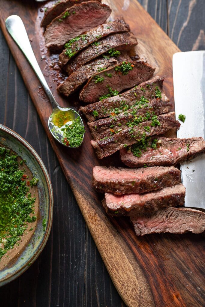 flat iron steak with chimichurri sauce on a cutting board