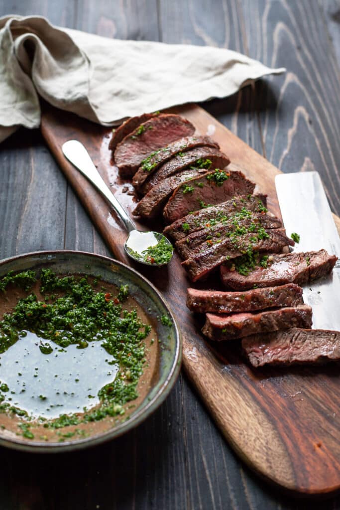 flat iron steak with chimichurri sauce on a cutting board