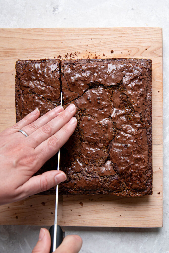 Hand cutting into a batch of brownies.