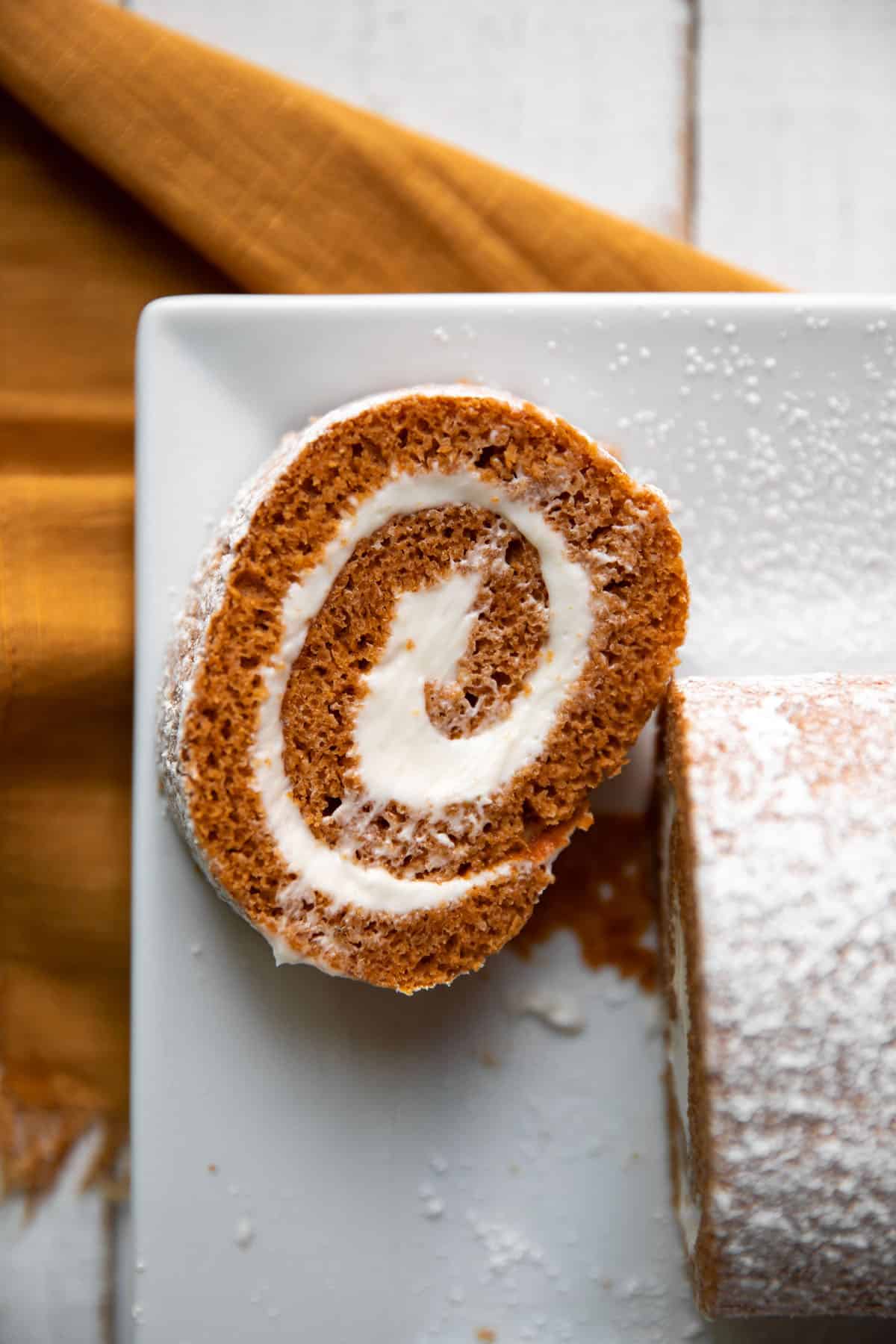 pumpkin roll log with cream cheese frosting and powdered sugar on top
