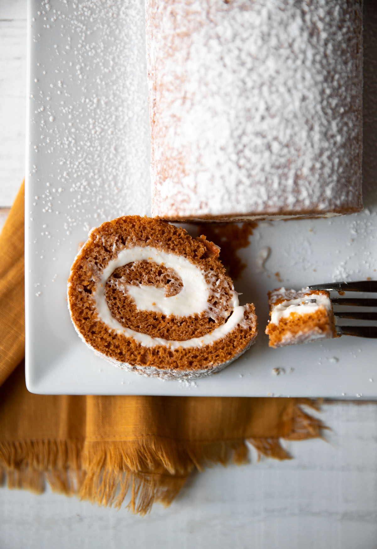 pumpkin roll log with cream cheese frosting and powdered sugar on top