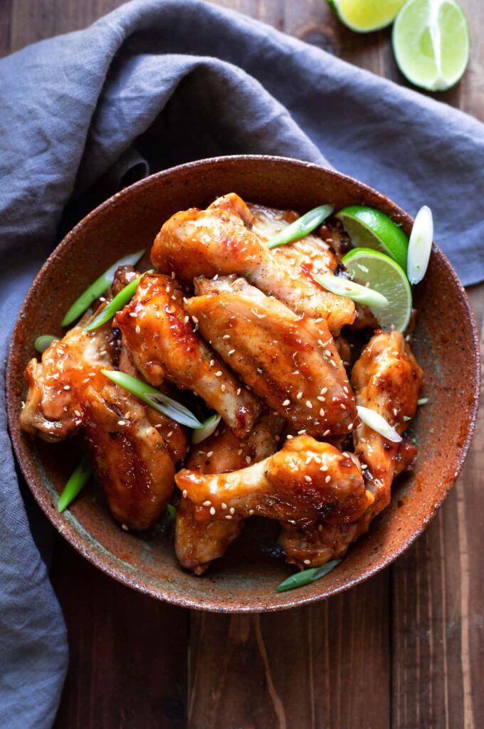 chicken wings tossed in an asian zing sauce with green onion and lime wedges in a bowl