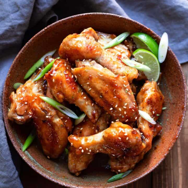 chicken wings tossed in an asian zing sauce with green onions and lime wedges in a bowl