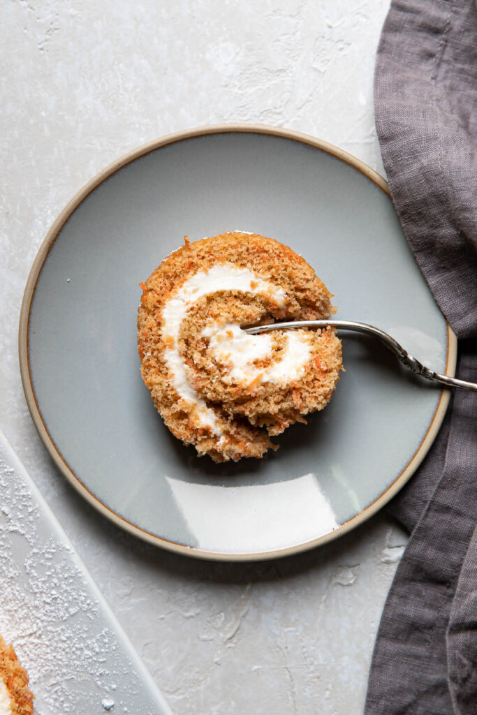 Carrot cake roll on a plate with a fork cutting in to it.