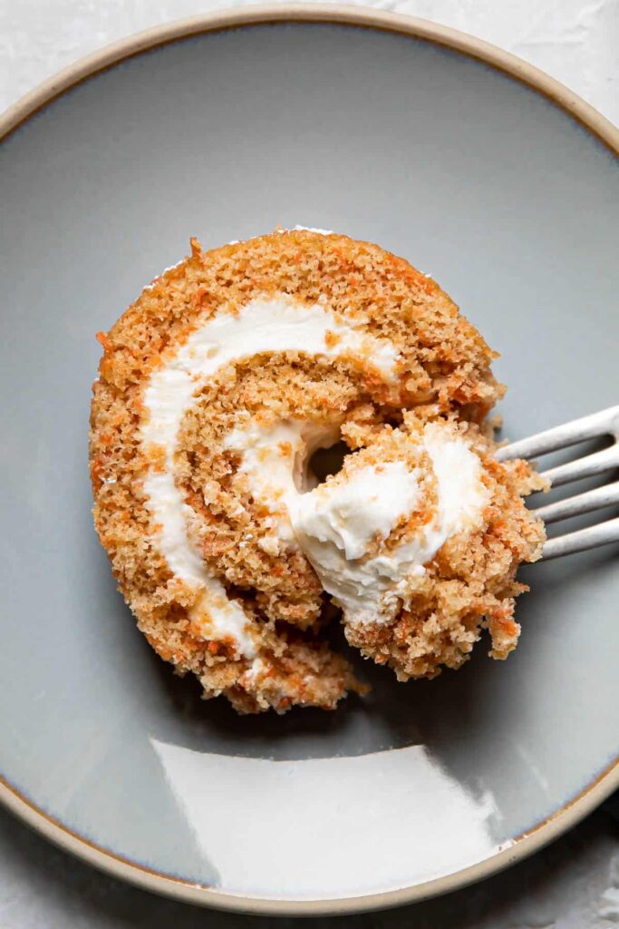 Fork holding a piece of carrot cake roll on a plate.