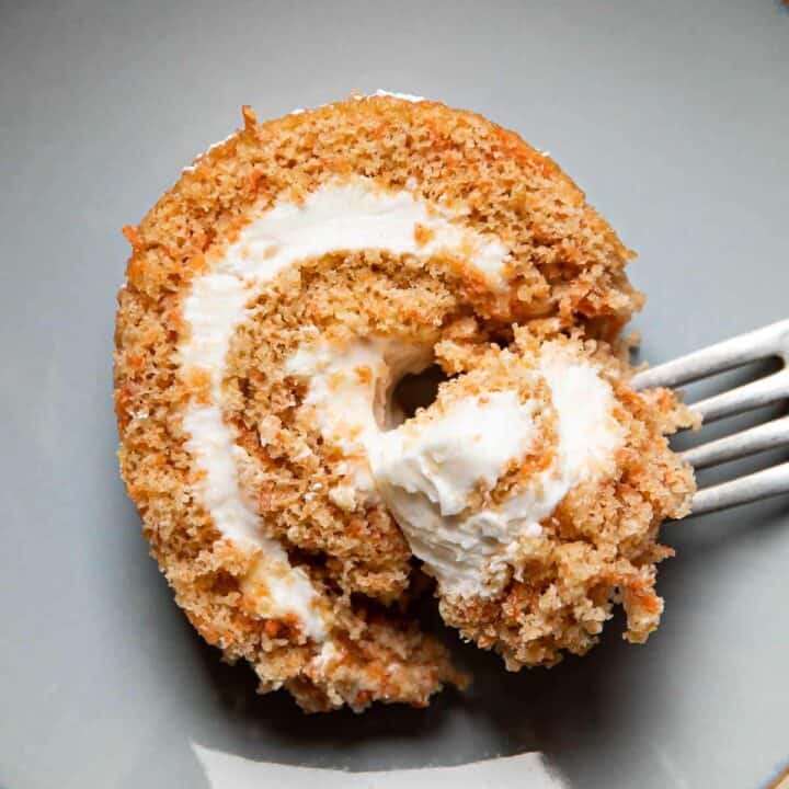 Fork holding a piece of carrot cake roll on a plate.