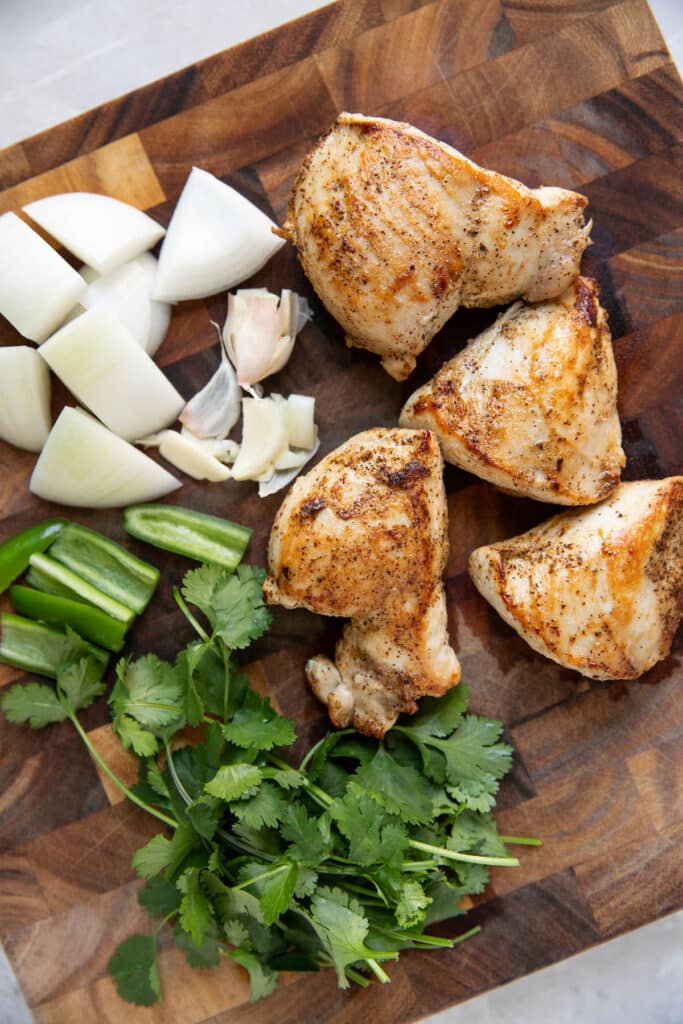 chicken on a cutting board with cilantro jalapeno and onions