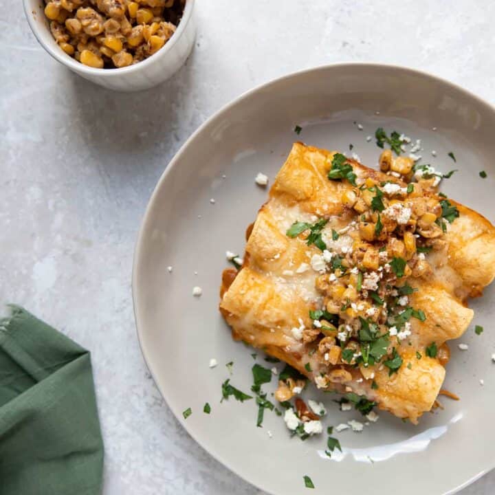 plate of crock pot chicken enchiladas with cilantro cotija cheese and elote corn