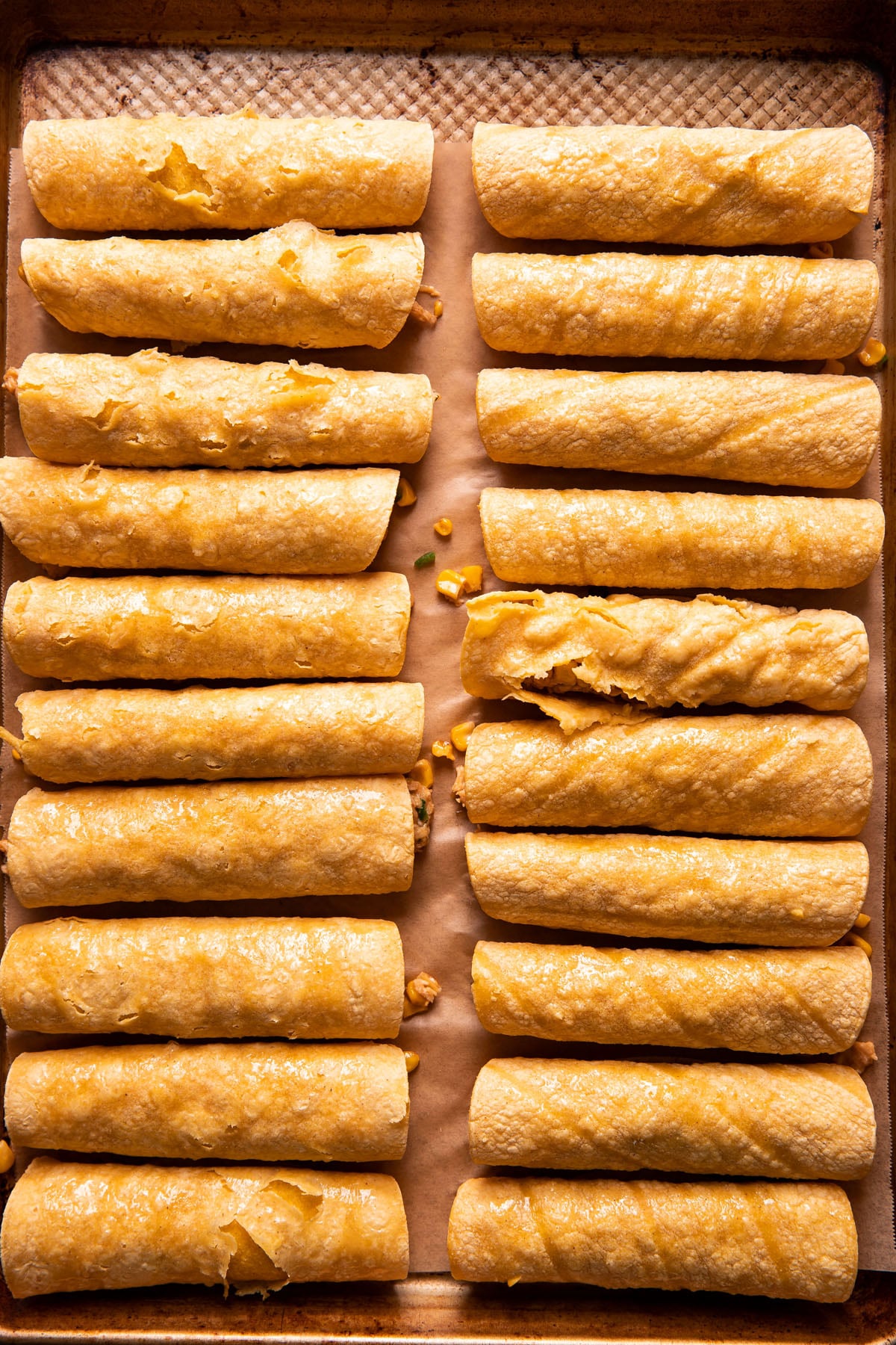 two rows of taquitos on a baking sheet before being baked