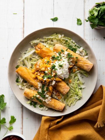 plate of taquitos filled with chicken and mexican corn served with lettuce and sour cream on top