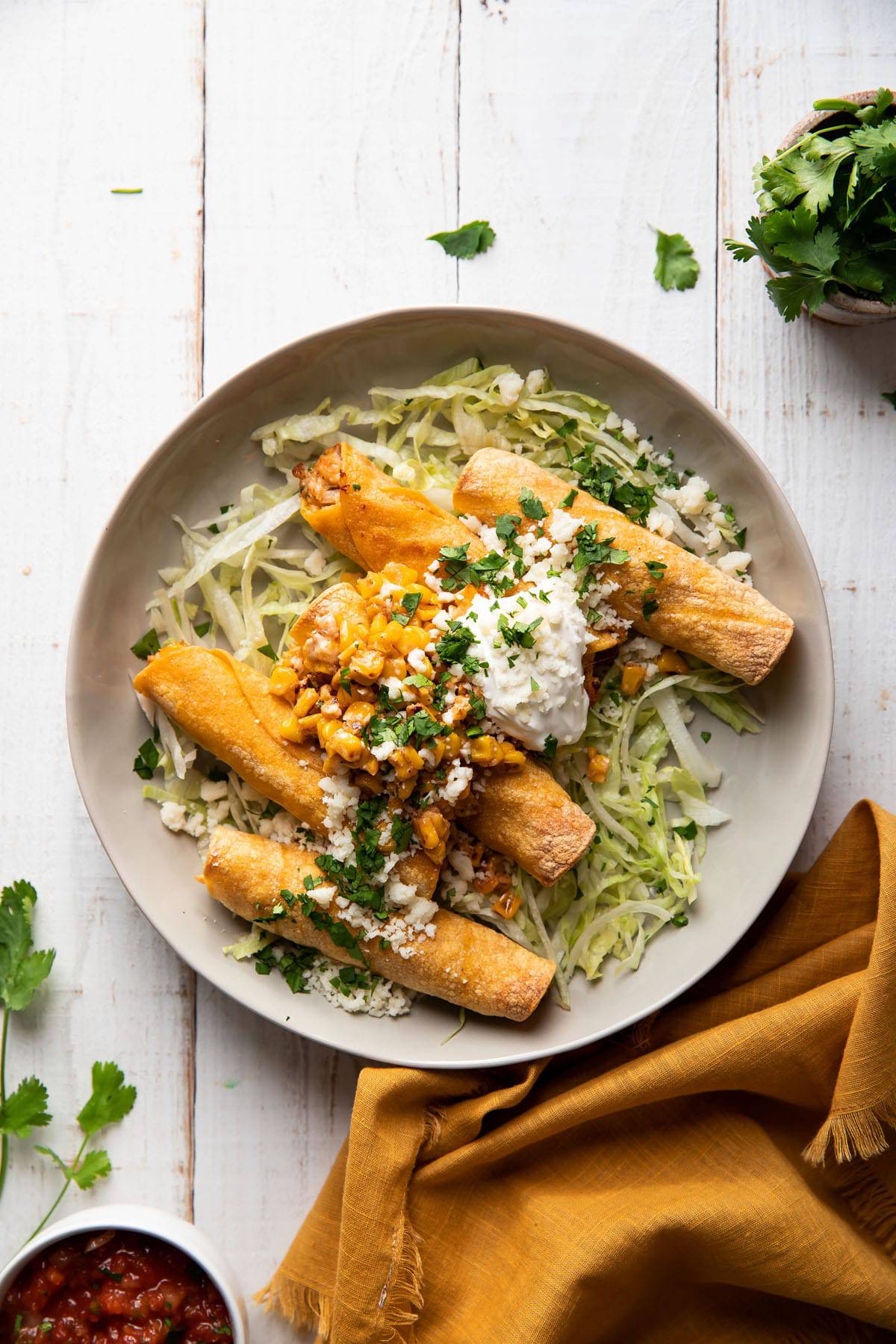 plate of taquitos filled with chicken and mexican corn served with lettuce and sour cream on top