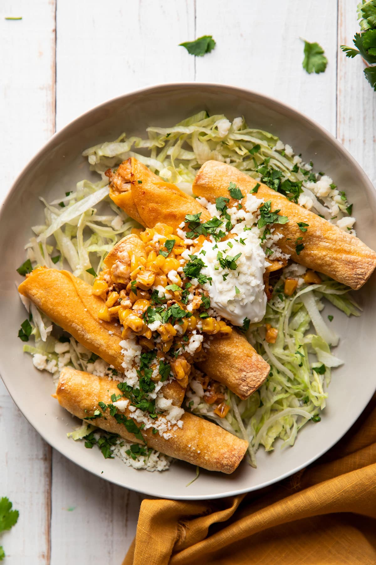 plate of taquitos filled with chicken and mexican corn served with lettuce and sour cream on top