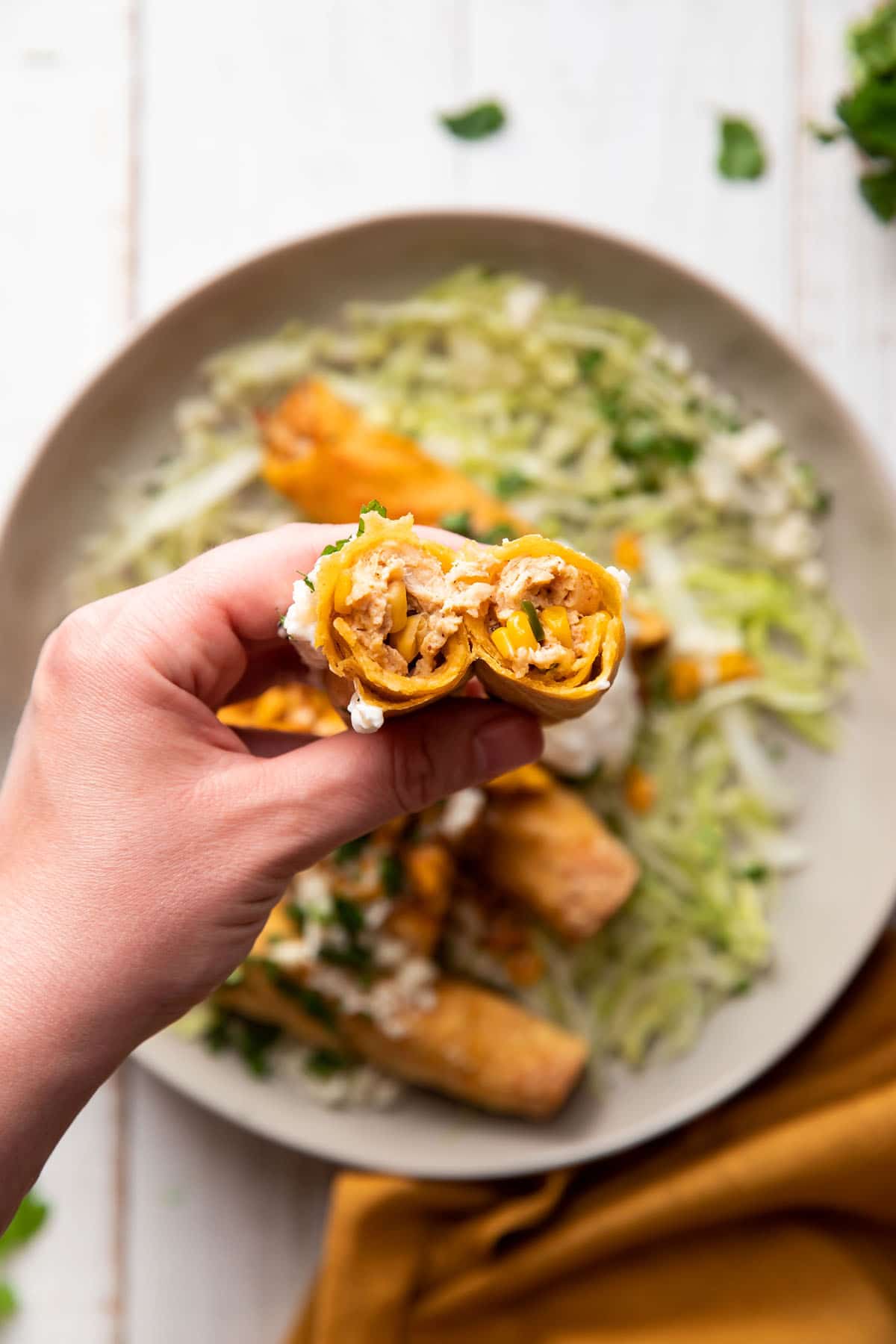 hand holding a taquito broken into half showing the chicken and corn on the inside