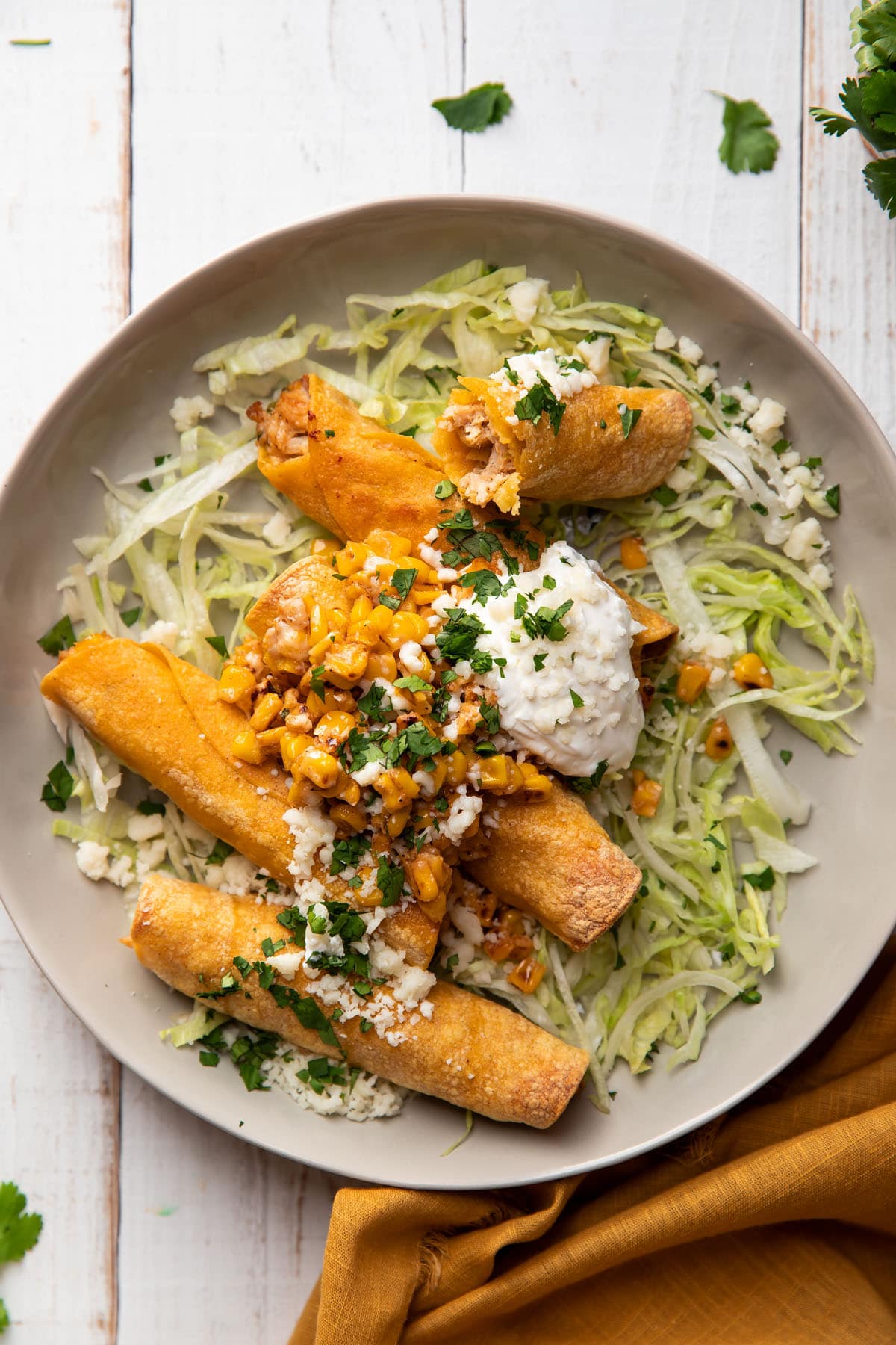 plate of taquitos filled with chicken and mexican corn served with lettuce and sour cream on top