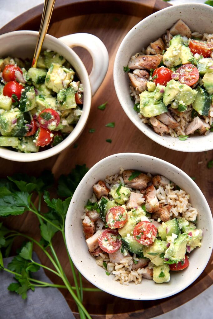 greek marinated chicken thighs with brown rice and avocado feta dip in bowls