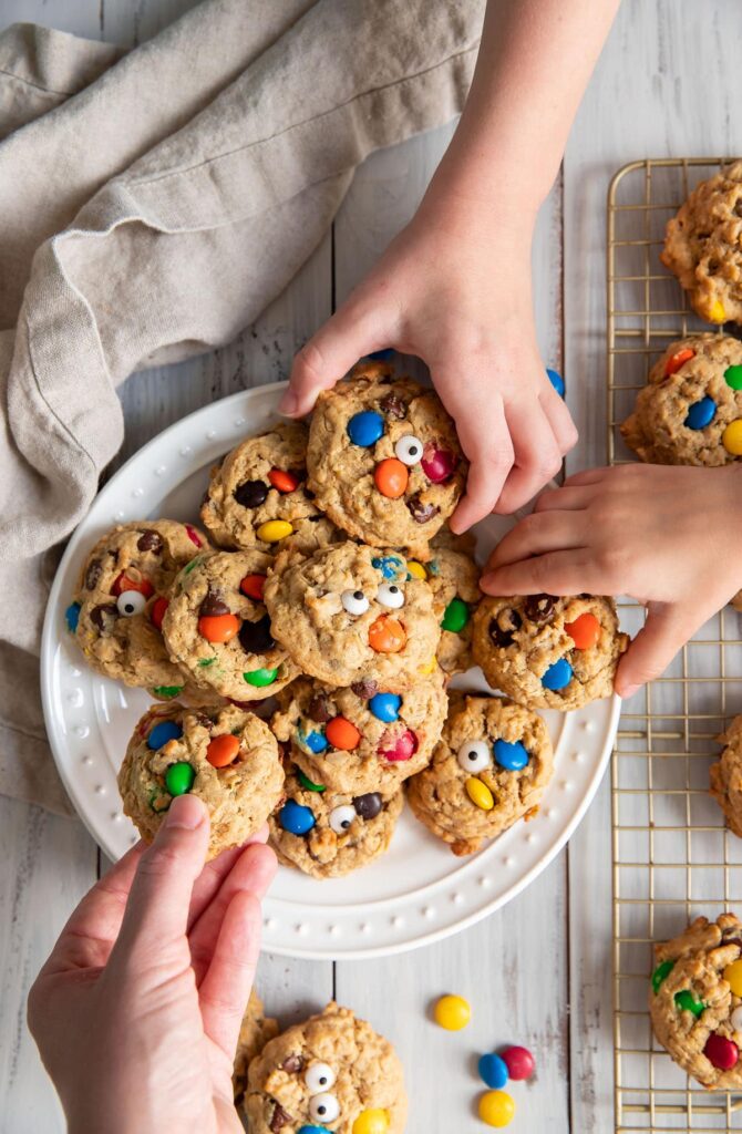 3 hands reaching for monster cookies on a plate