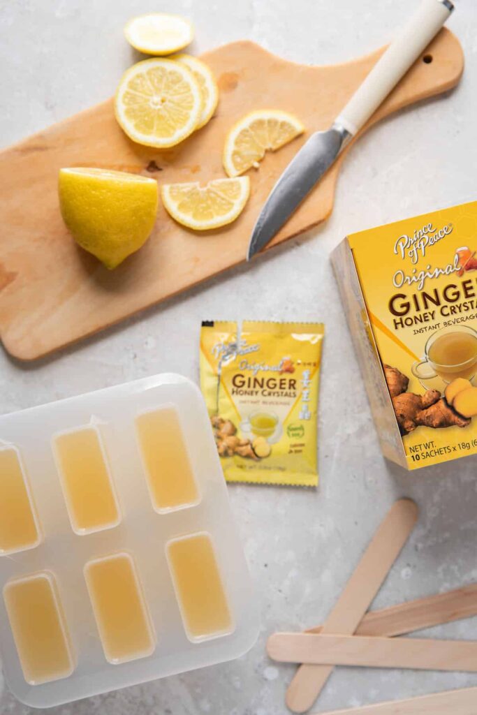 popsicle mold filled with lemonade and ginger tea next to a cutting board with lemons and a tea box