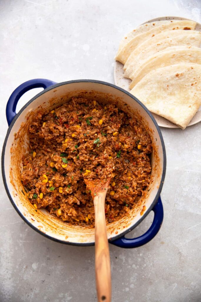 mexican beef and rice in a cast iron pot with tortillas on the side