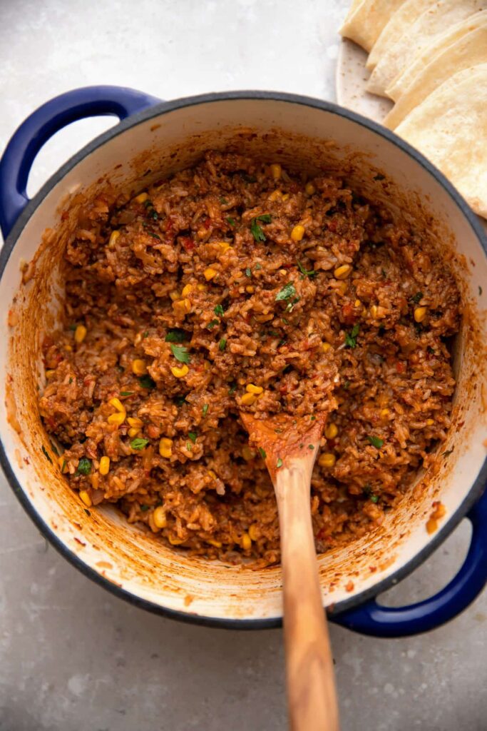 mexican beef and rice in a cast iron pot with tortillas on the side