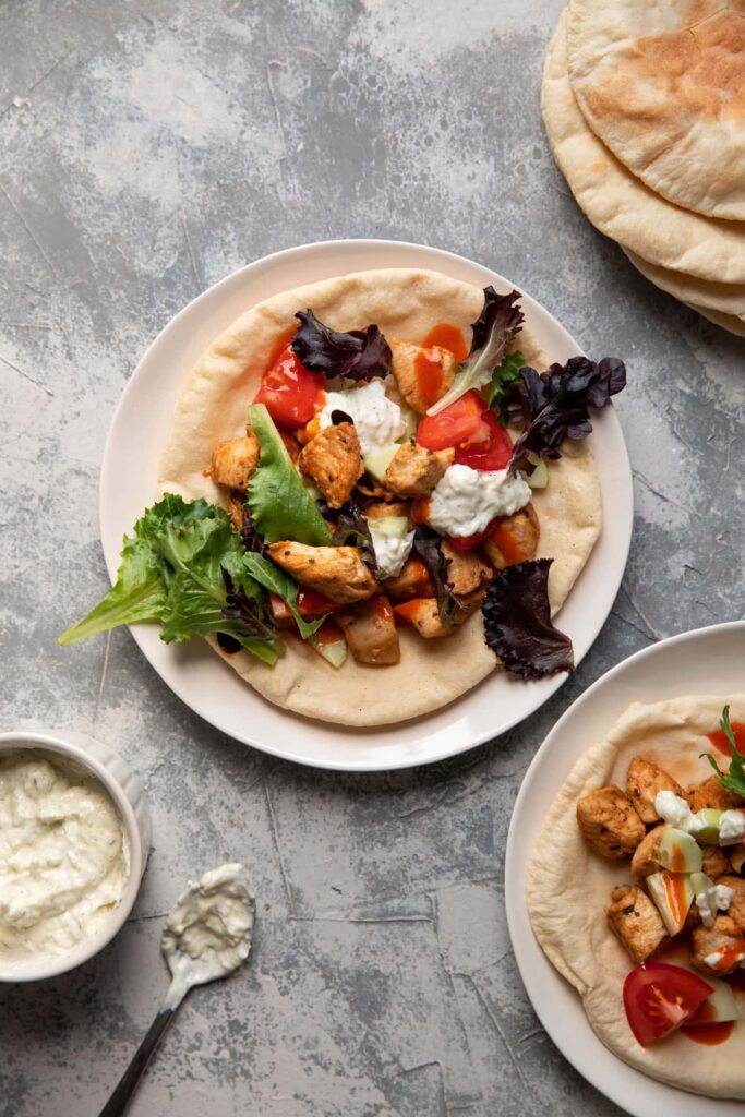 chicken pitas on a plate with tomato lettuce and tzatziki sauce