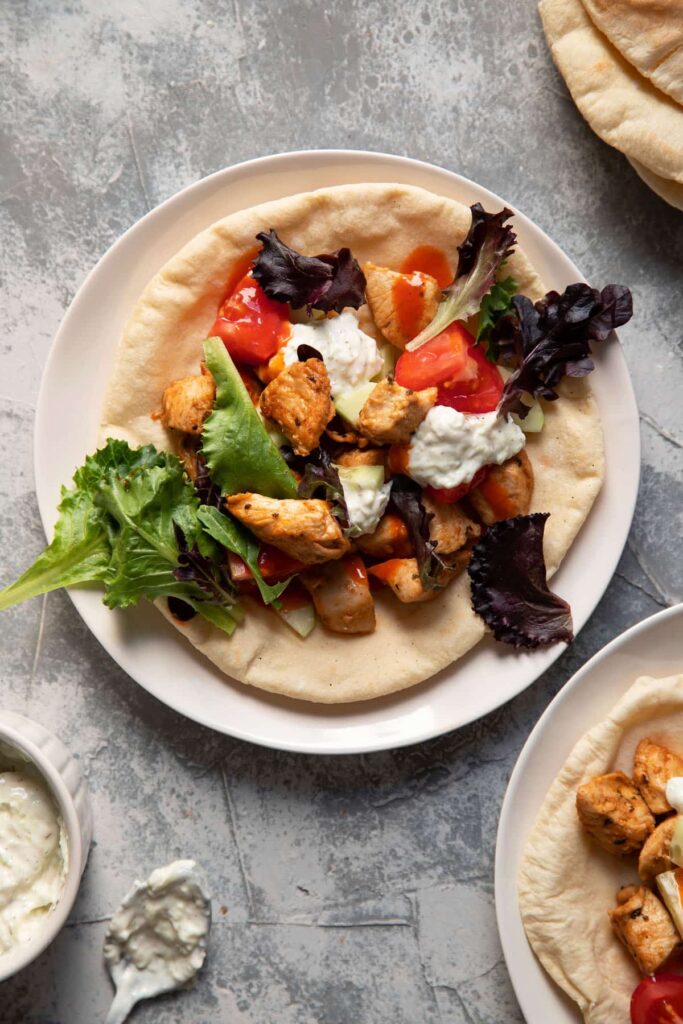 chicken pitas on a plate with tomato lettuce and tzatziki sauce