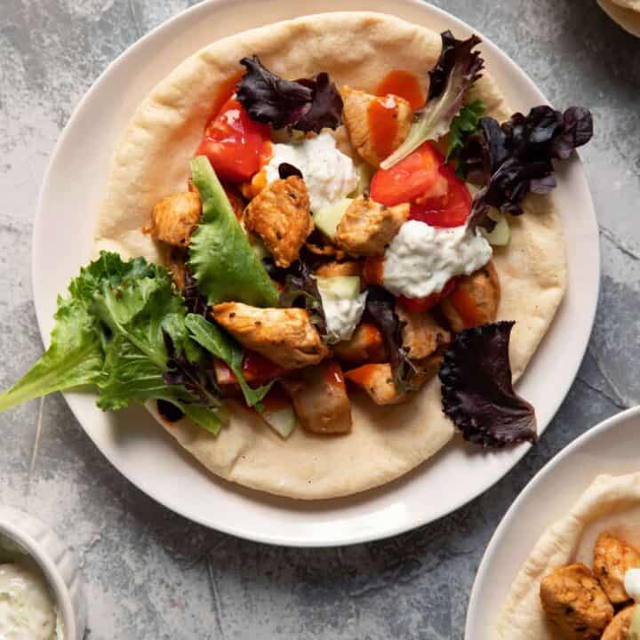 chicken pitas on a plate with tomato lettuce and tzatziki sauce