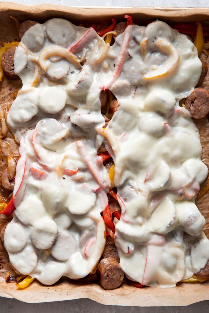 sliced italian sausages with bell peppers and melted cheese on a sheet pan