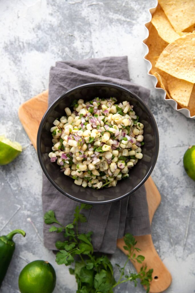 white corn salsa with red onions and peppers in a grey bowl
