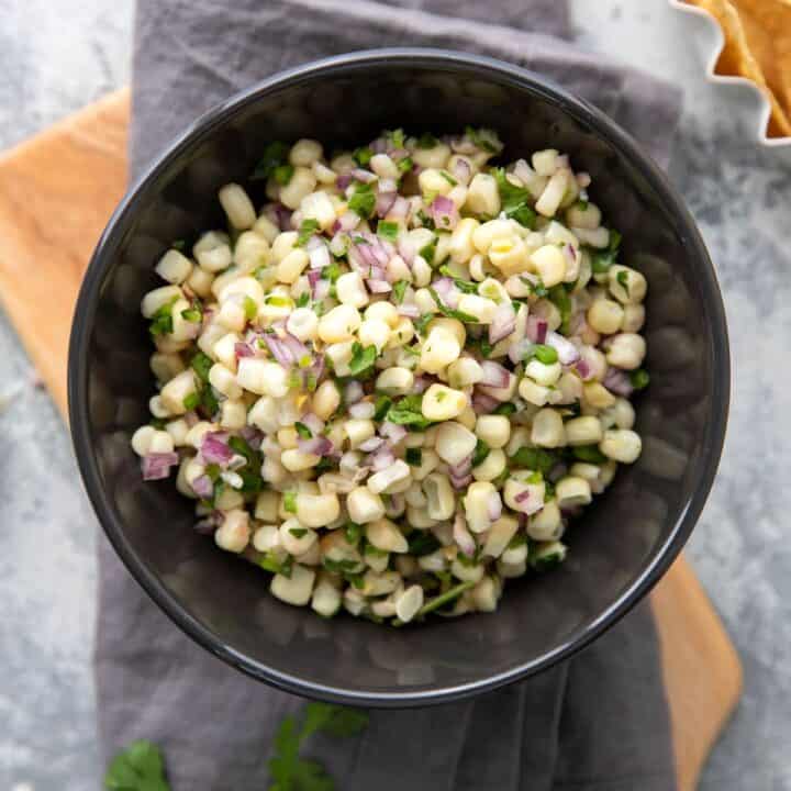 white corn salsa with red onions and peppers in a grey bowl