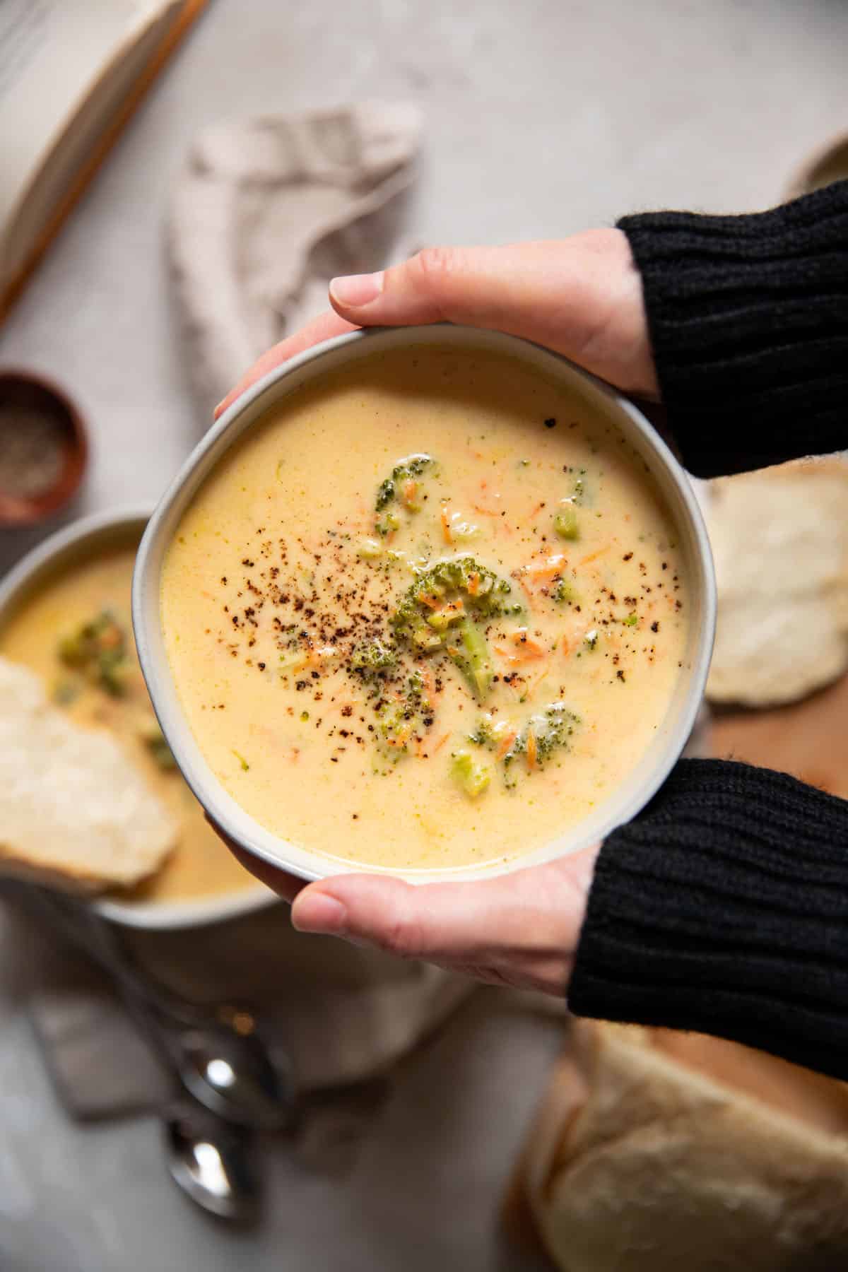 hands holding a bowl of broccoli cheese soup