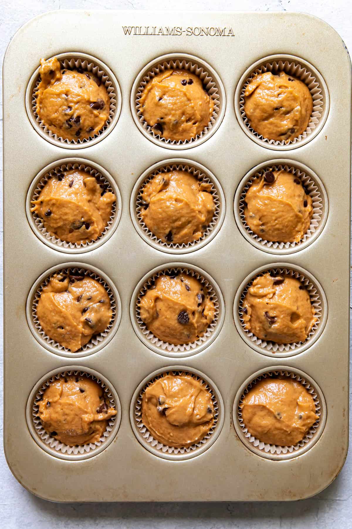 pumpkin chocolate chip muffins before baking, in a muffin tin.